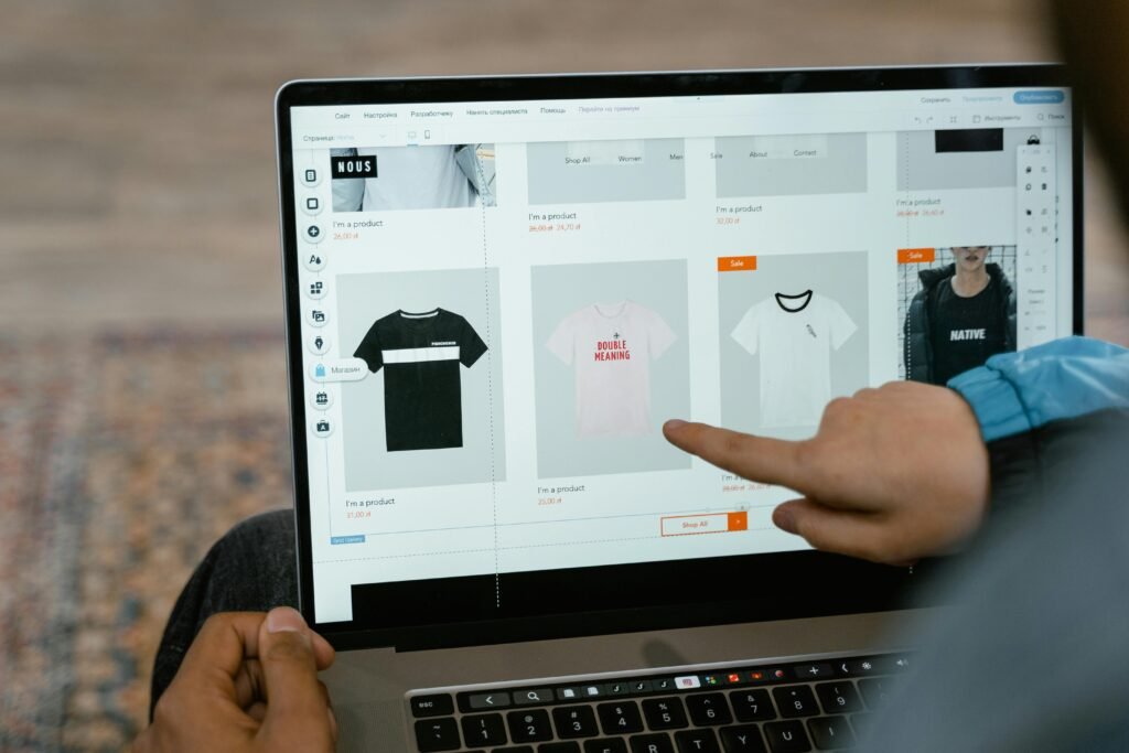 Home A person points to t-shirt options in an online store on a laptop screen.