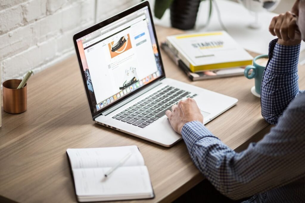Person working on a laptop with a notebook at a bright desk