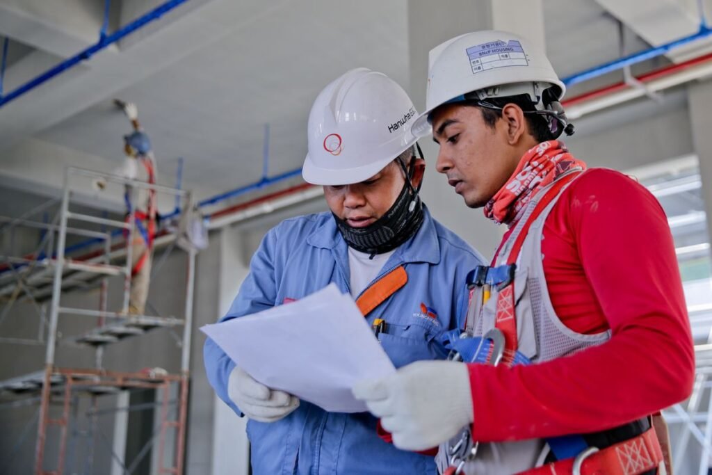 Two construction workers in hard hats reviewing building plans on site