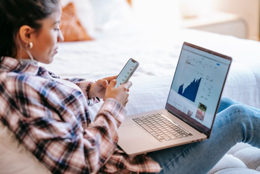 Person using a phone and laptop with performance charts on screen