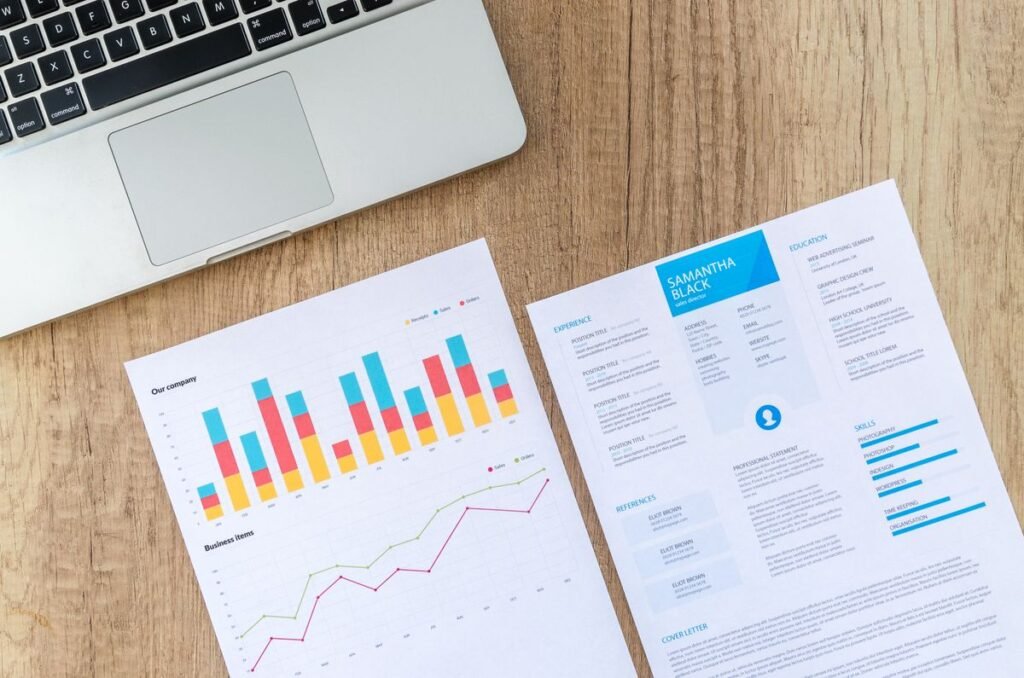 Laptop beside printed bar charts and reports on a wooden desk